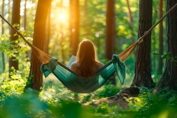 A person enjoying a relaxing afternoon reading in a hammockWoman reclining in hammock, engrossed in book, amidst trees and nature